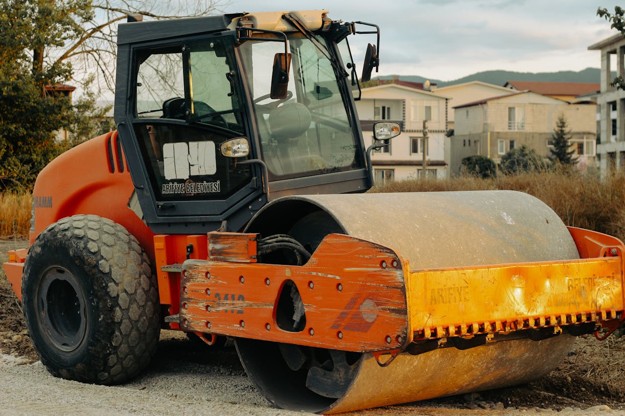 Meist A large orange construction roller parked outdoors, ready for roadwork tasks.